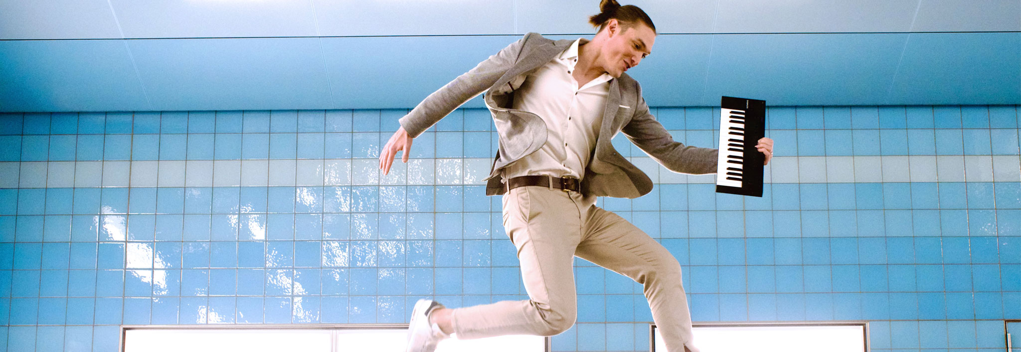 Andreas Langsch. Klavierkabarettist. Künstler in einem U-Bahnhof fotografiert, springt dynamisch hoch und hält ein ein kleines Keyboard unterm Arm.